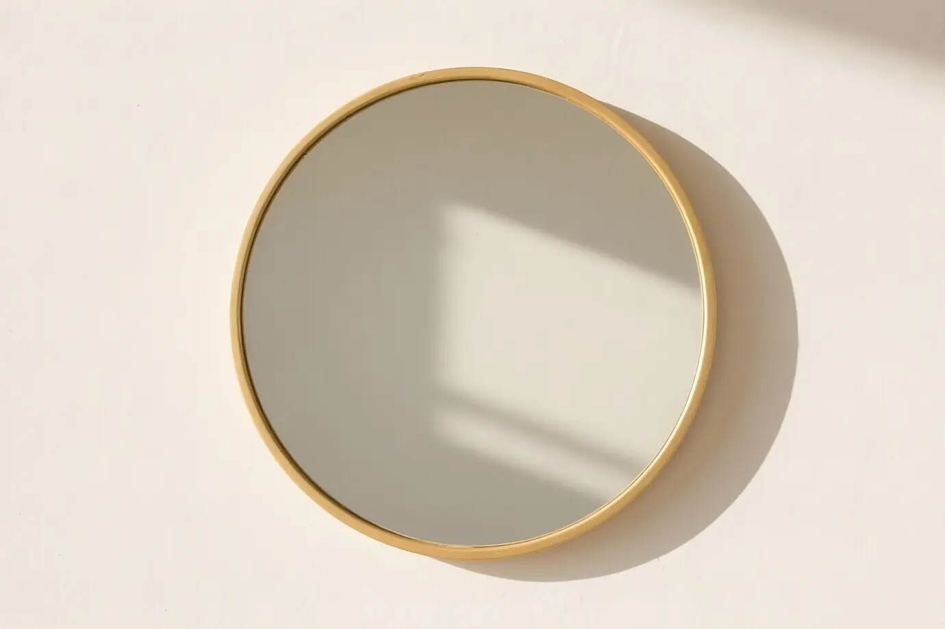 Runder Spiegel mit goldenem Rahmen an weißer Wand